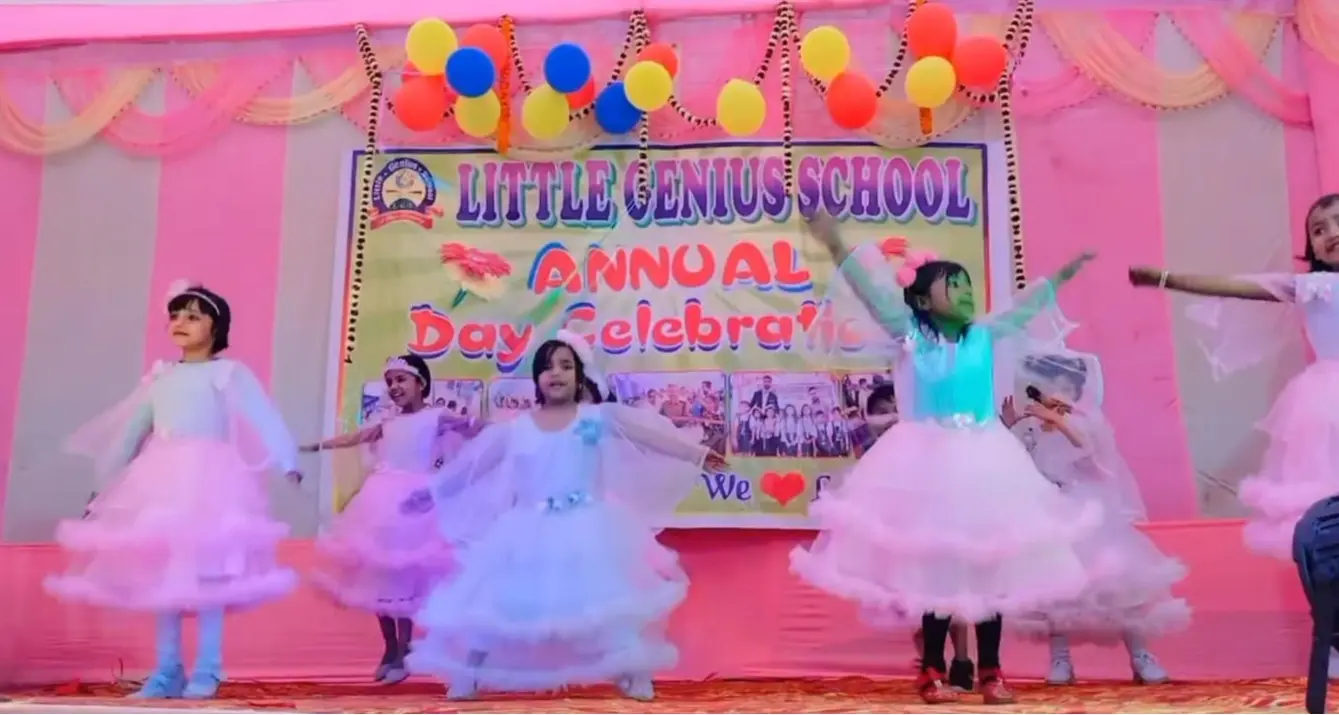 Young girls in blue tops and pink tutu skirts dance on a balloon-decorated stage.