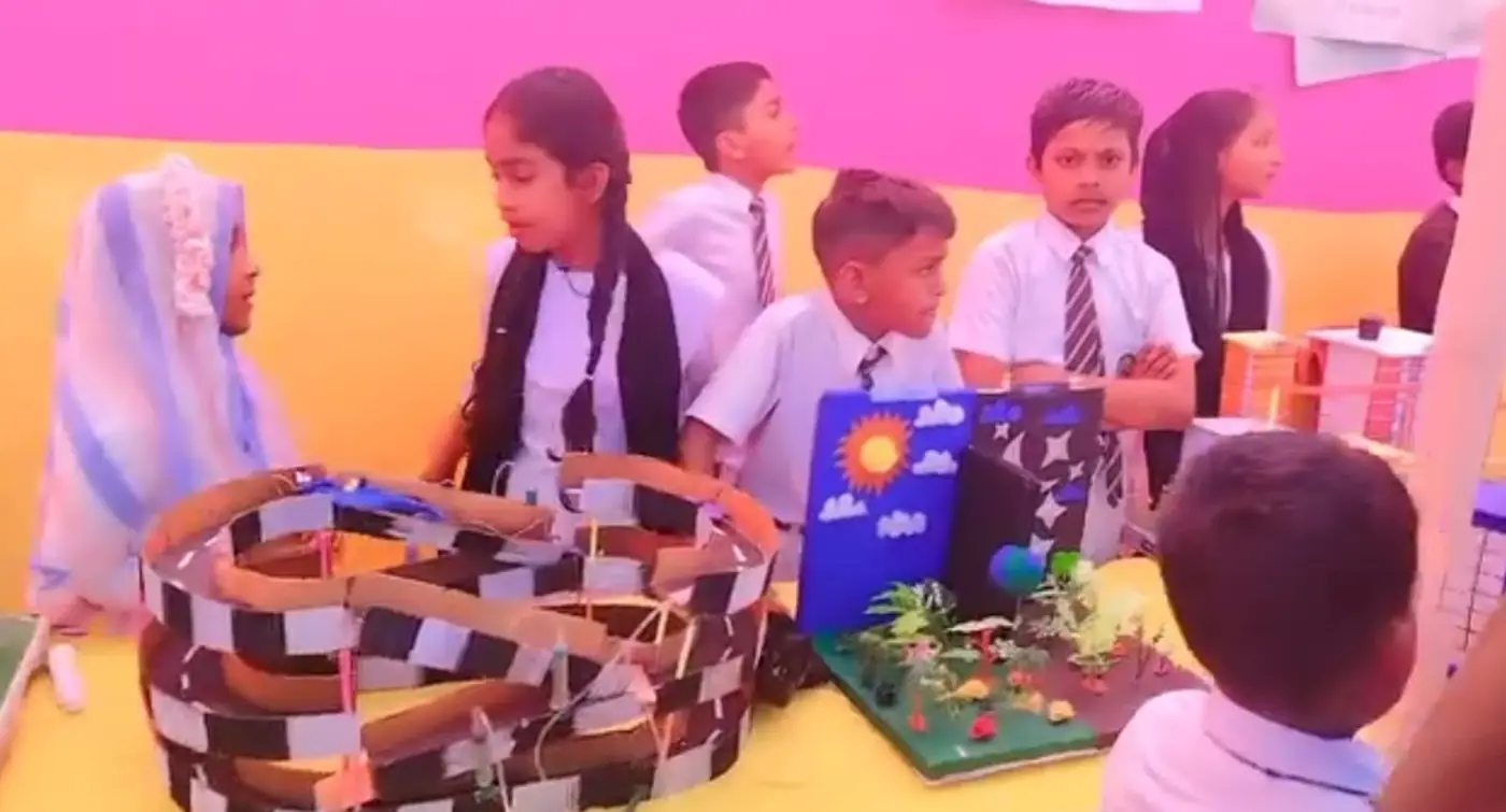Students stand behind handmade models of a spiral track and a day-and-night display.
