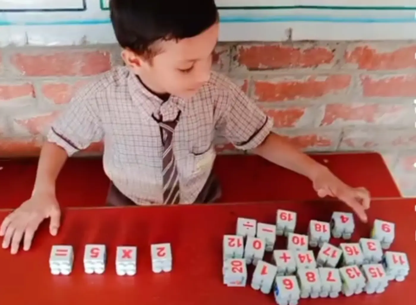 A boy in uniform builds a multiplication equation with numbered interlocking blocks.