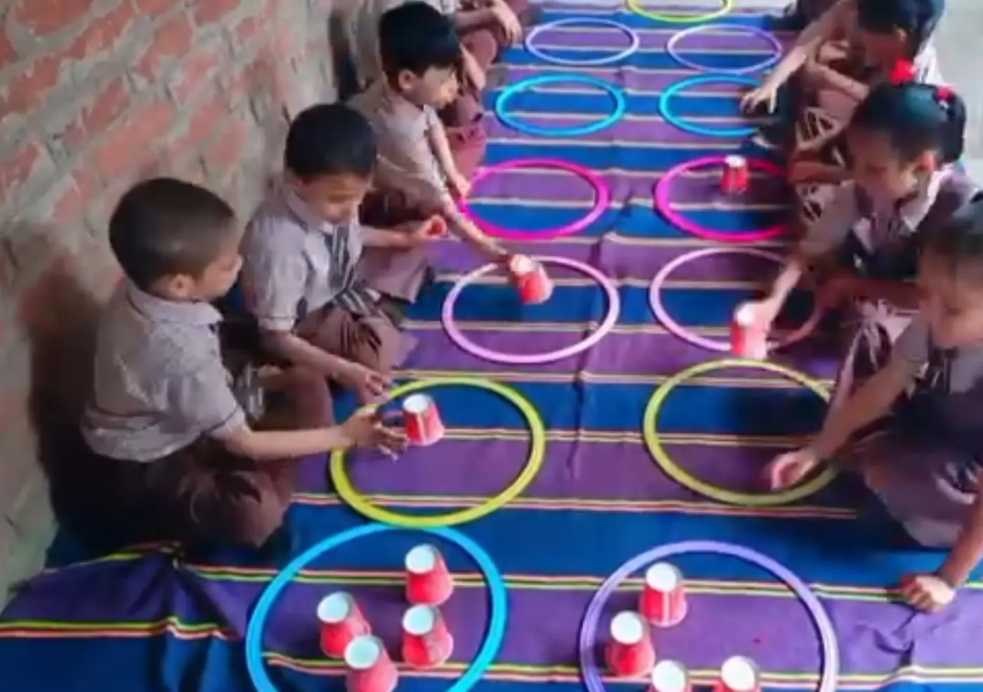 Young students place patterned cups inside colorful plastic hoops on a striped rug.