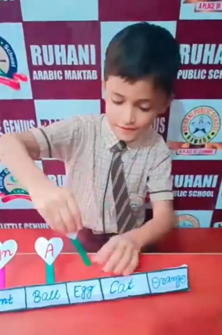 A boy matches a heart-shaped letter stick to handwritten words on a classroom table.