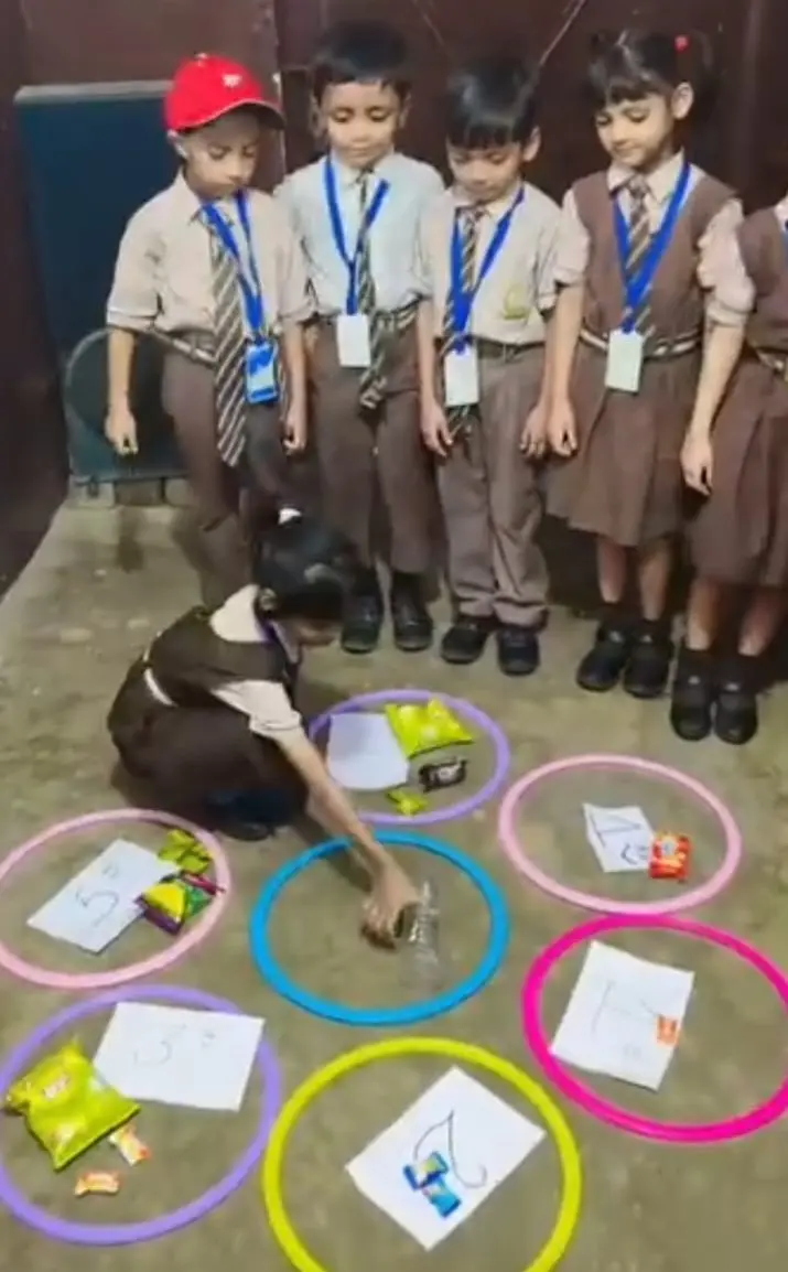 Students gather around numbered hula hoops on the floor during a counting activity.