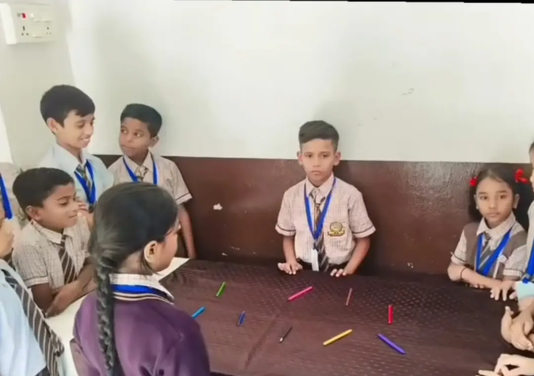 Primary students gather around a table covered with colorful pencils for shared work.