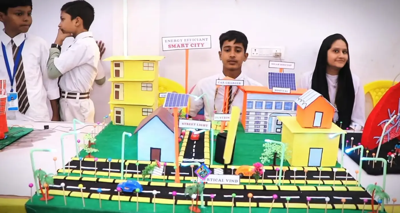 Students present a model city with solar panels and streetlights labeled smart city.