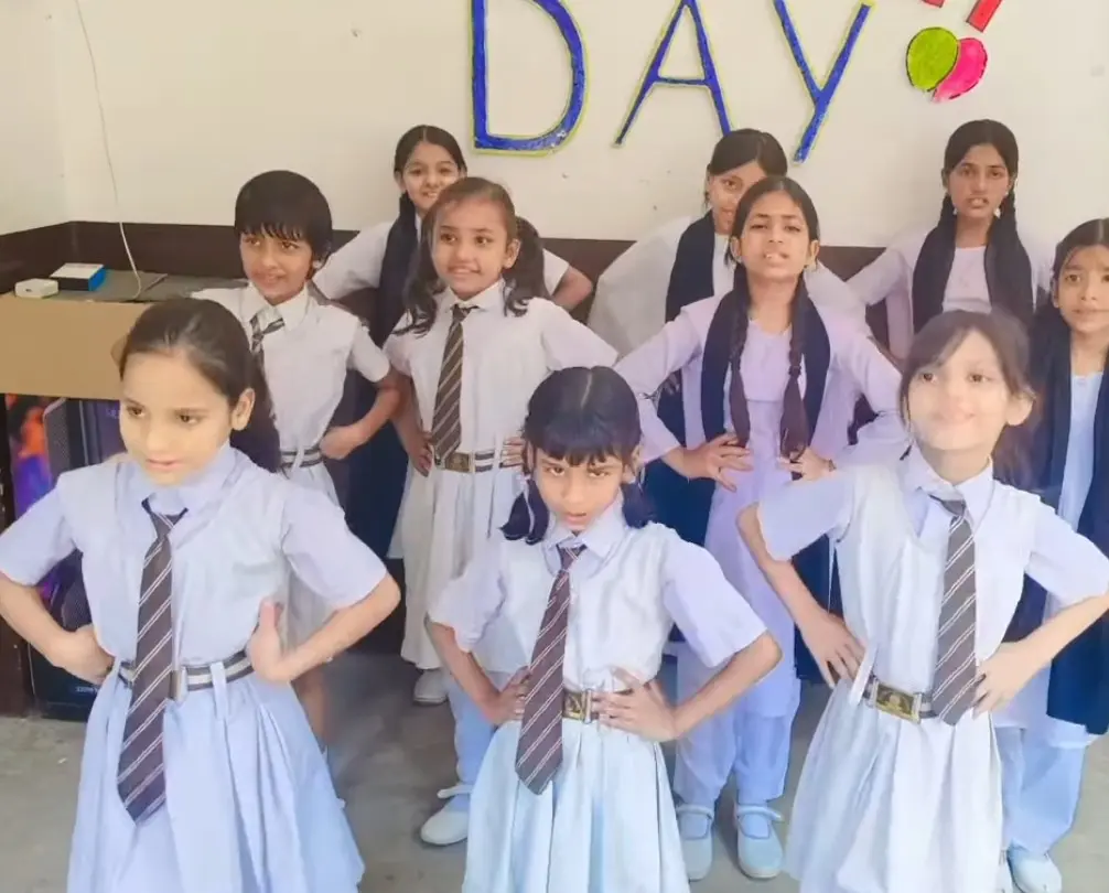 Girls in school uniforms pose with hands on hips during a choreographed indoor performance.
