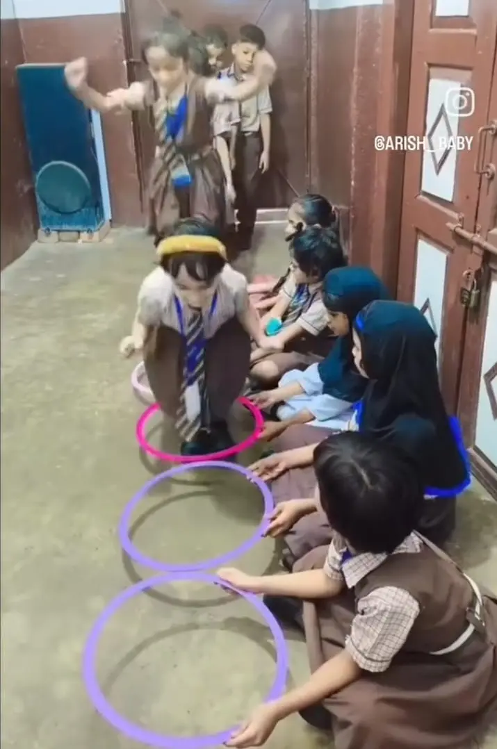 A girl in uniform jumps through colorful hula hoops while classmates watch.