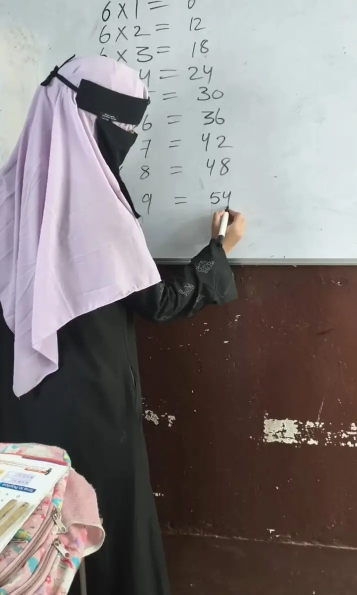 A student writes the six times table on a classroom whiteboard.