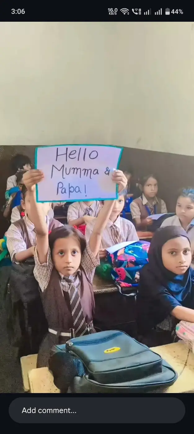 A girl in school uniform holds up a handmade sign reading Hello Mumma and Papa.