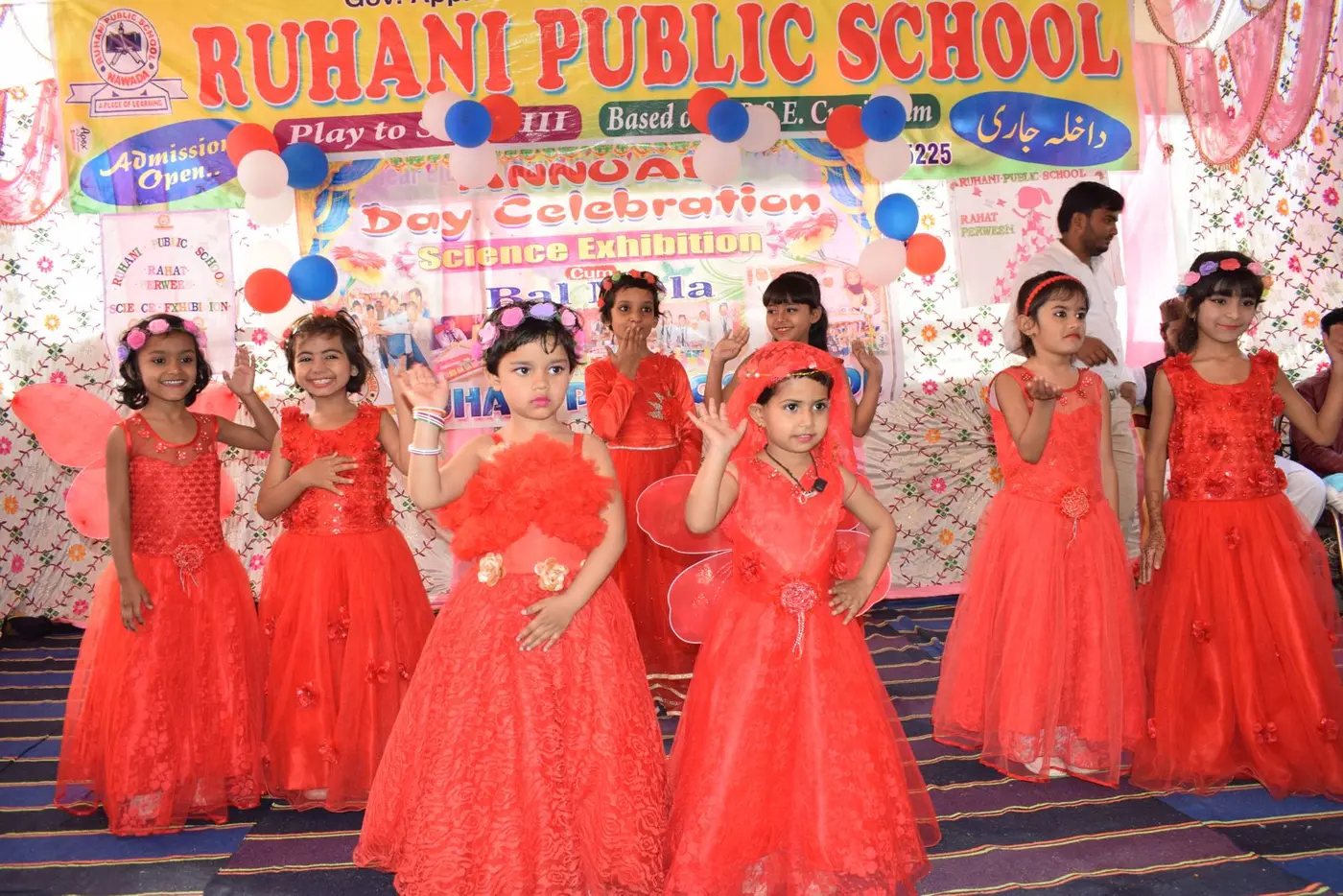Girls in bright red tulle dresses dance on stage before an Annual Day banner.