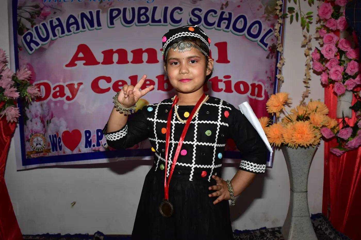 A young performer with a medal poses with a peace sign before an Annual Day banner.
