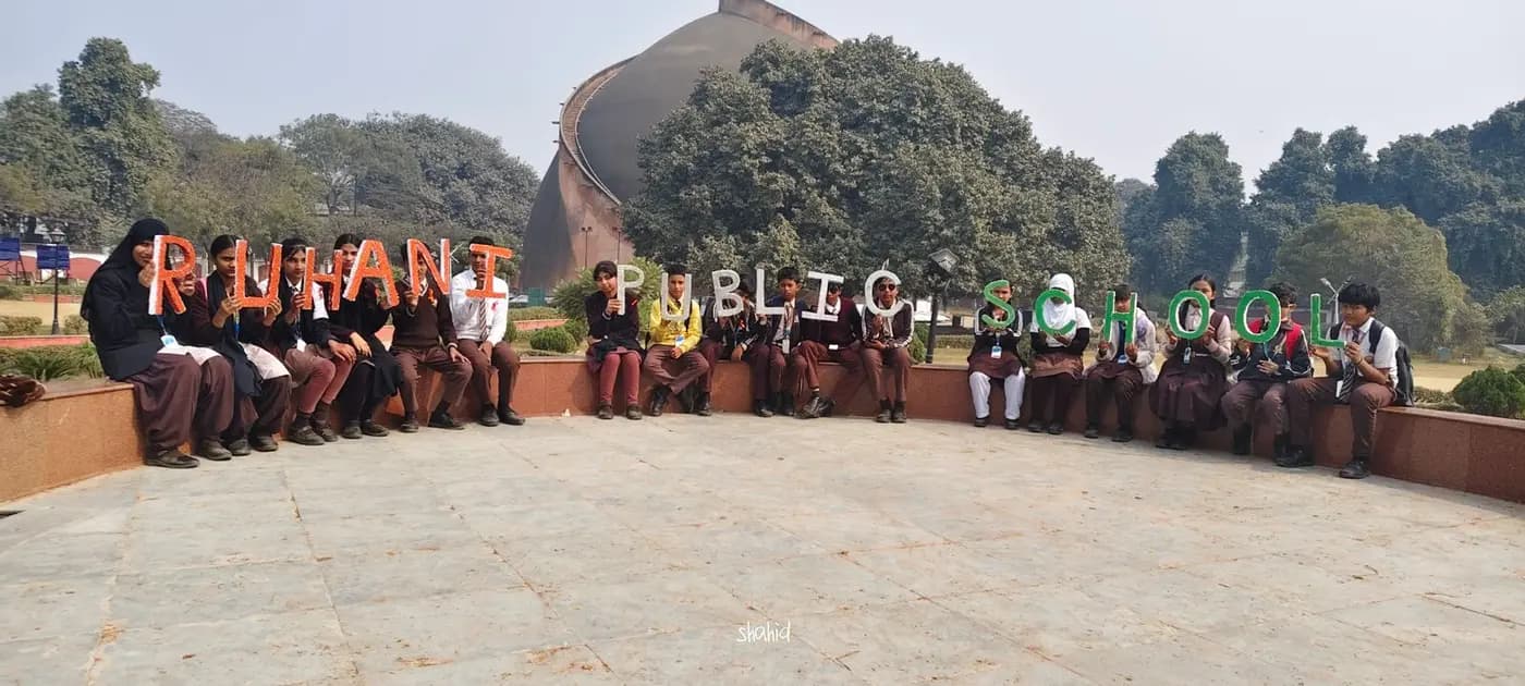 Students sit outdoors holding colorful cut-out letters that spell Ruhani Public School.
