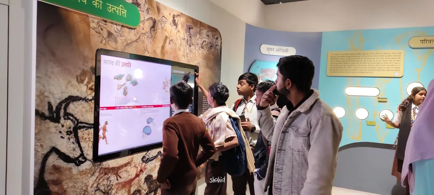 Students and a teacher explore an interactive human evolution exhibit in a museum.