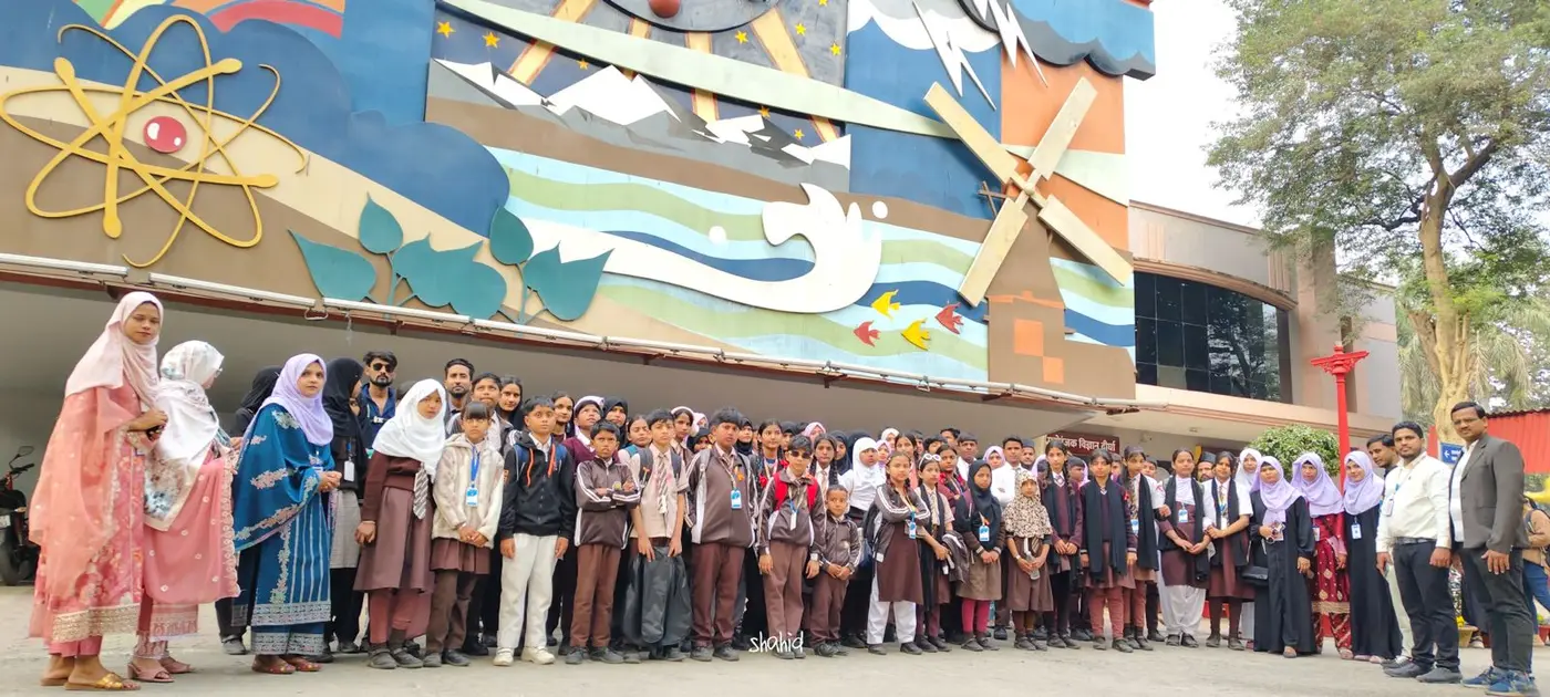 Students and teachers pose in front of a colorful science-themed mural.