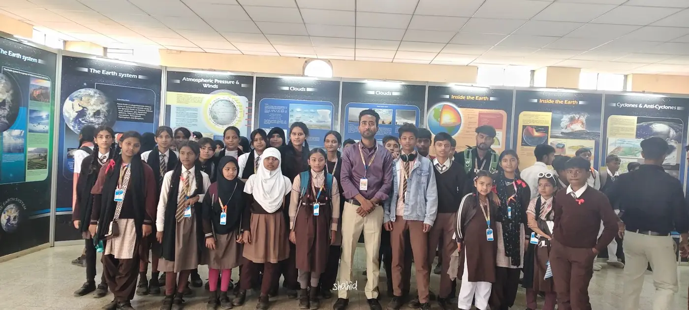 Students and a teacher pose before educational posters about Earth systems and weather.